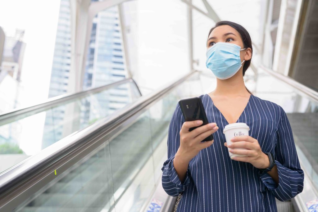 Woman holding phone, wearing face covering and social distancing to prevent COVID-19 spread