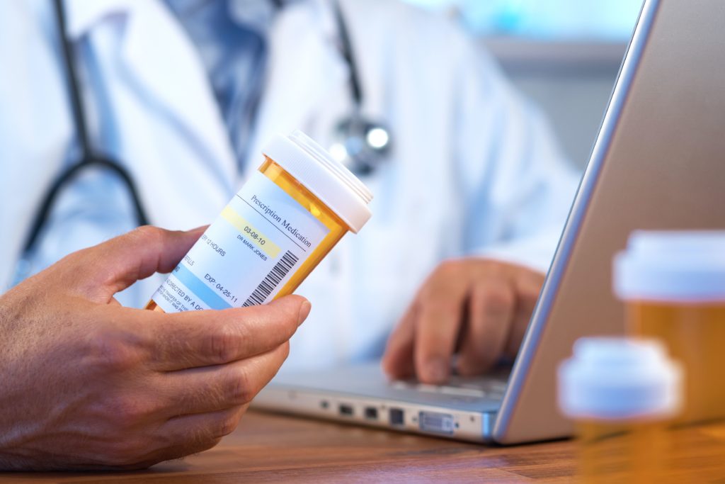 Doctor using laptop for telehealth visit to discuss medication with patient.