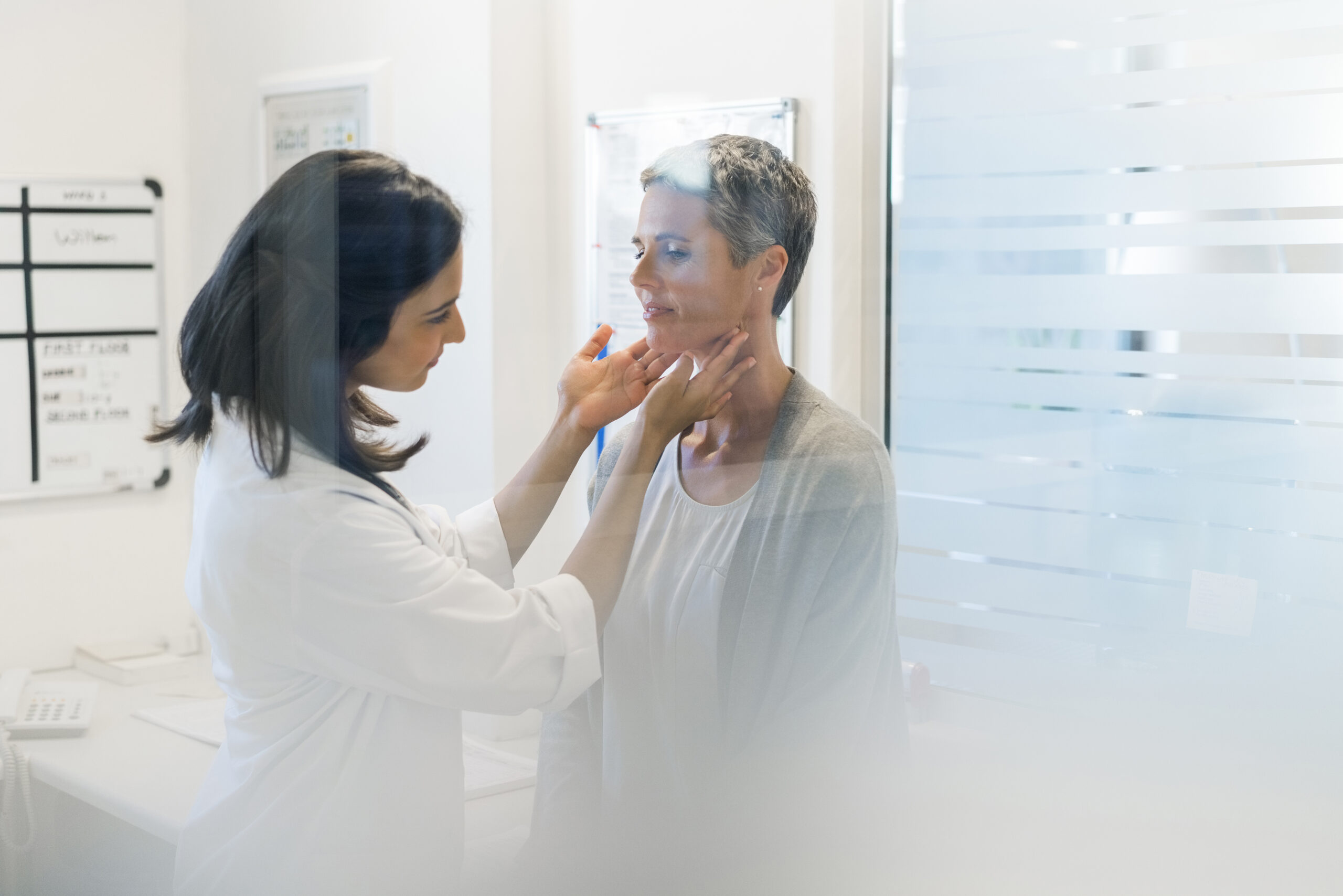 Doctor examining patient's thyroid glands. Female practitioner is wearing lab coat. They are in hospital.