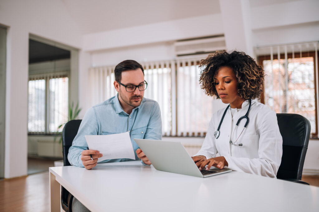 Office Manager discussing paperwork with doctor on laptop.